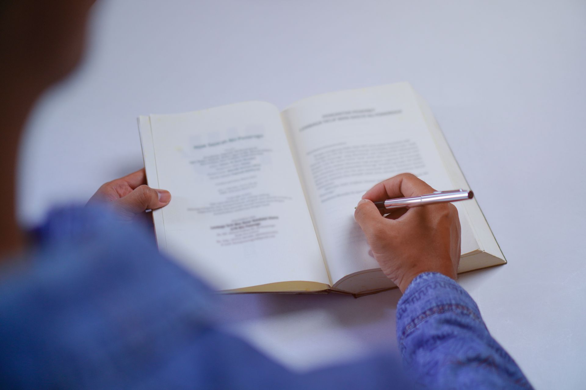 A person is writing in a book with a pen.
