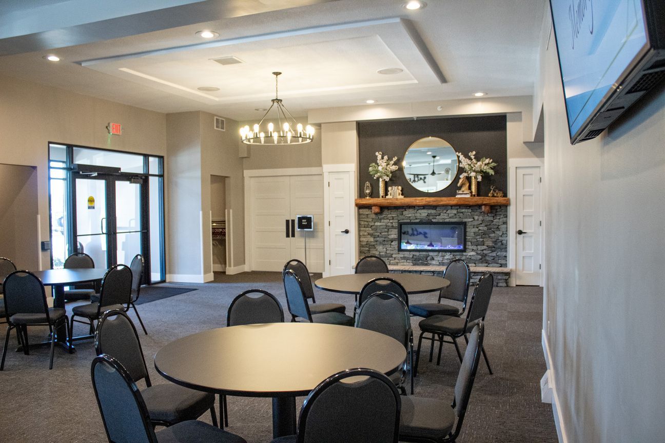 Elegant lounge with round tables, black chairs, chandelier, fireplace, and wall-mounted TV