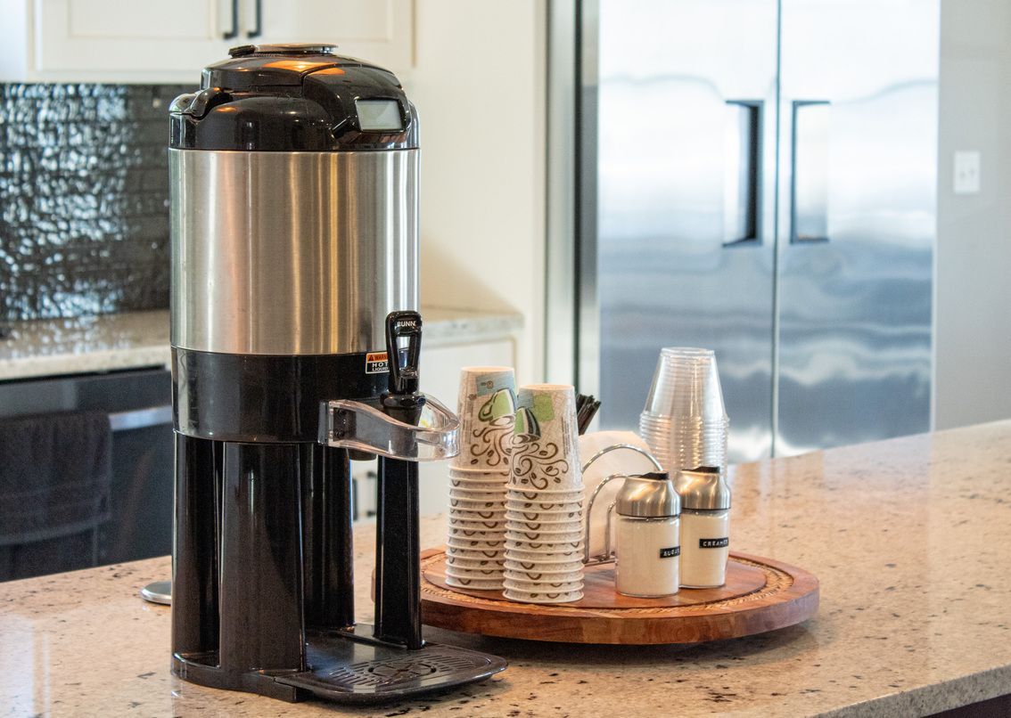 Coffee urn on kitchen counter with cups and condiments on a tray