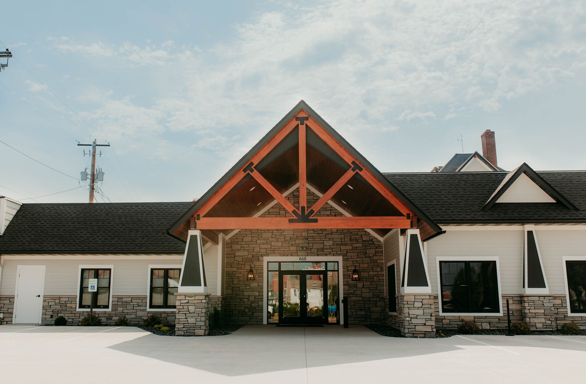 Front view of a stone lodge with a red timber roof and central glass entrance in a snowy setting