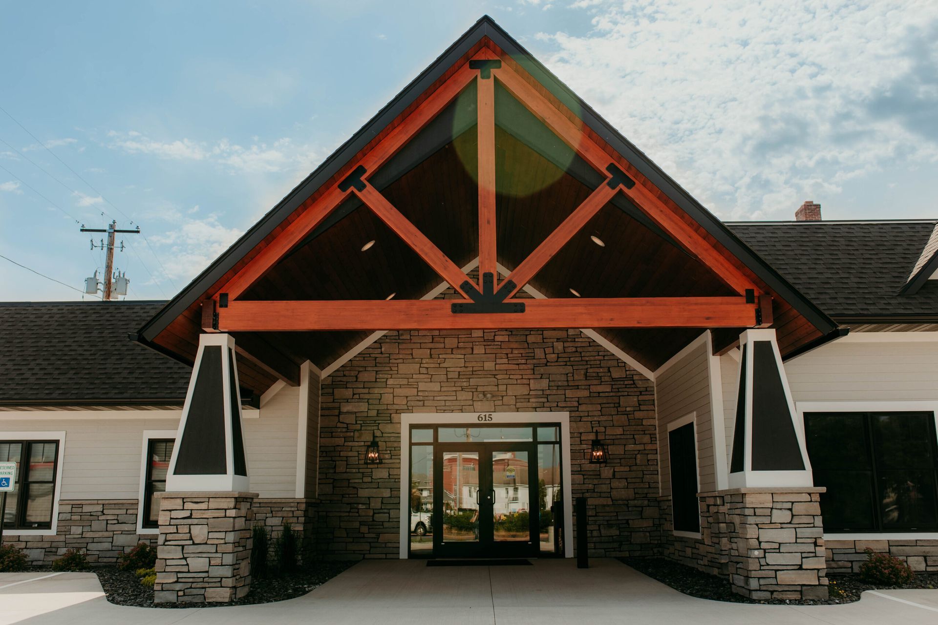 Stone building entrance with a peaked wooden roof and glass doors, viewed from the front.