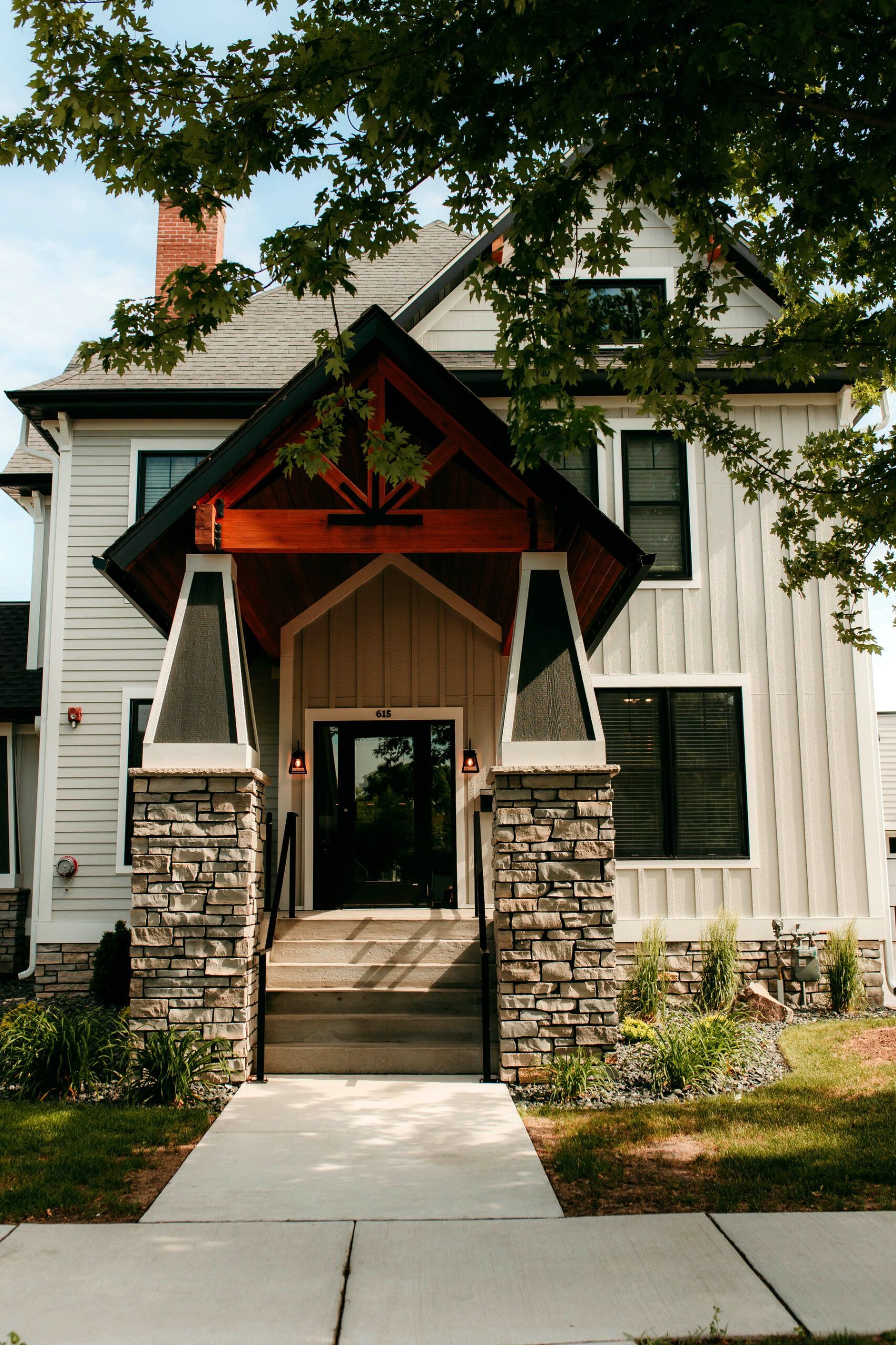 Front entrance of a white house with a steep gabled porch, stone columns, and a walkway