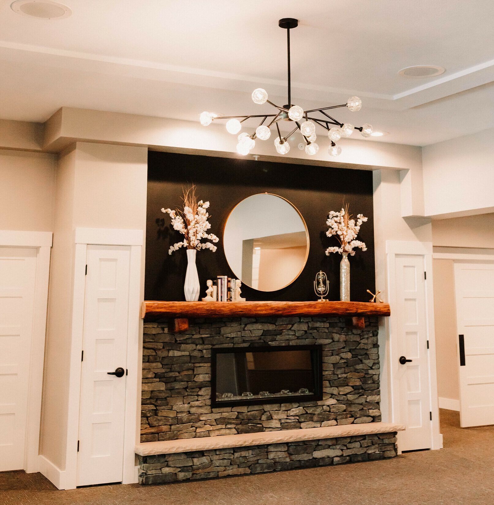 Living room fireplace with dark stone, mirrored mantel, white doors, and modern chandelier