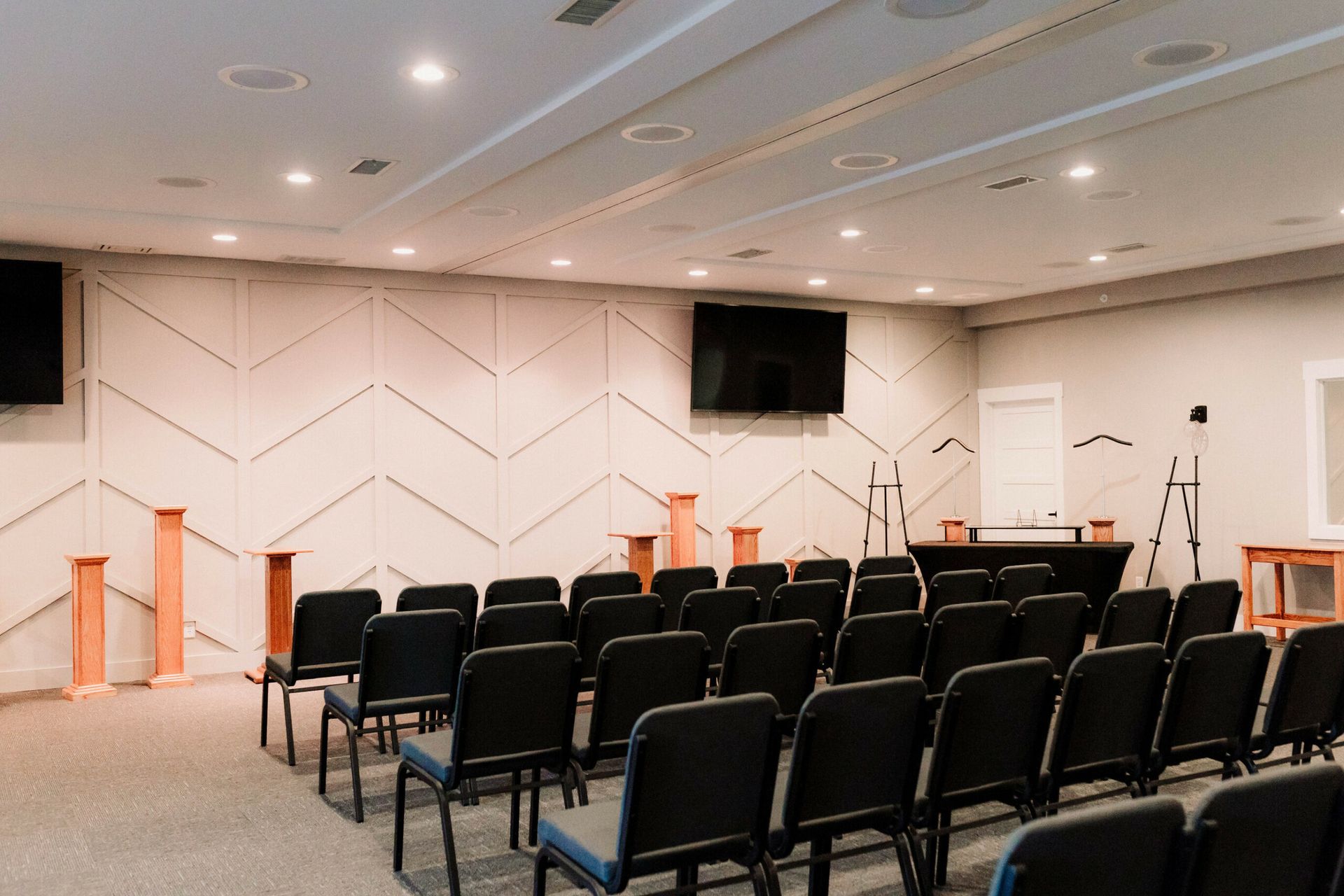 Empty conference room with rows of black chairs, podiums, and wall-mounted screens
