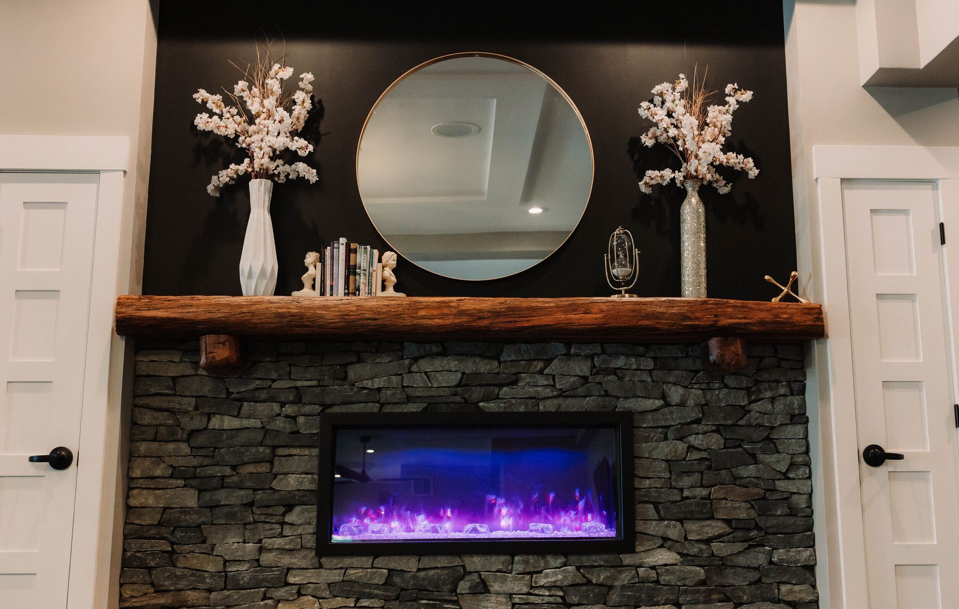 Stone fireplace with purple electric fire, wooden mantel, round mirror, and white floral decor