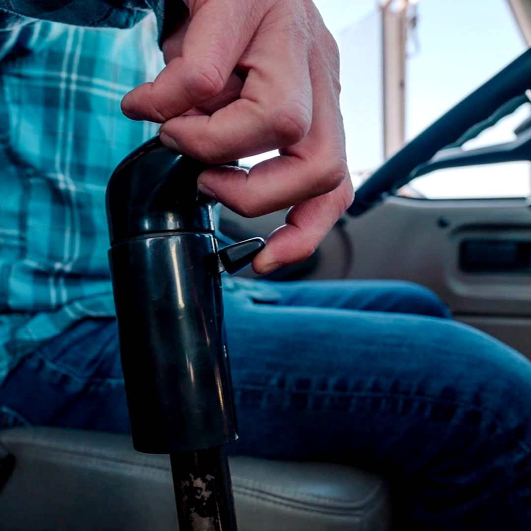 A man in a plaid shirt is holding a steering wheel and shifting in a semi truck