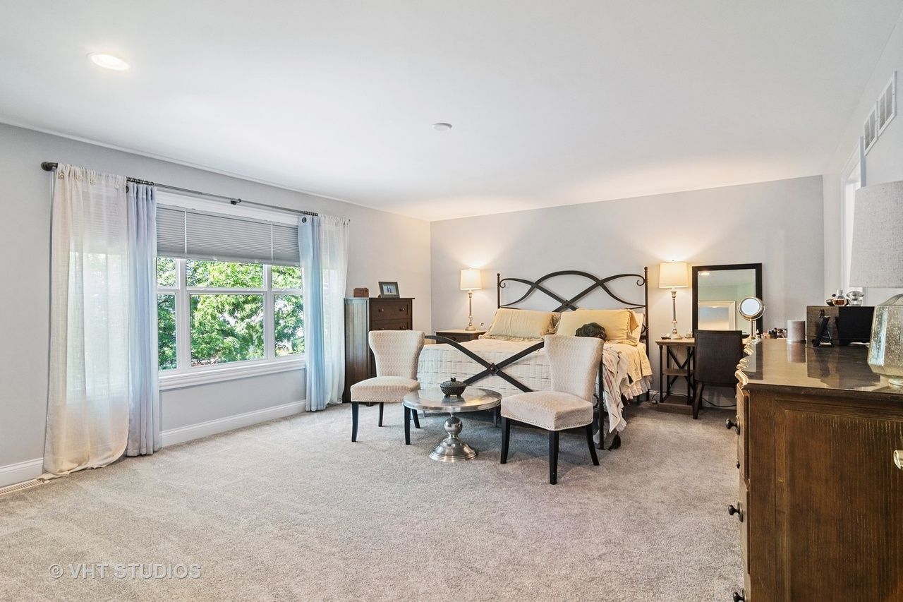 A bedroom with a large bed , dresser , chairs and a window.
