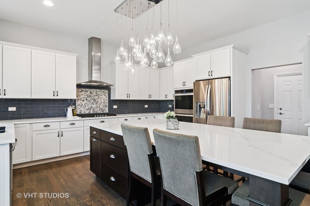 A kitchen with white cabinets , stainless steel appliances , a large island and a dining table.