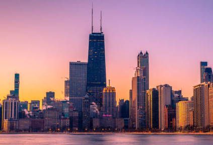 A city skyline at sunset with a lake in the foreground.