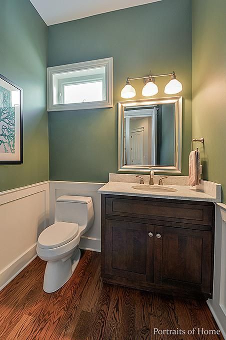 A bathroom with green walls , a toilet , sink and mirror.