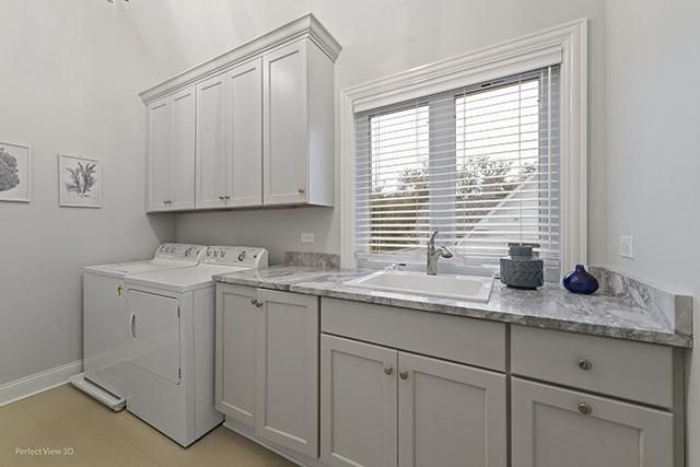 A laundry room with white cabinets , a washer and dryer , a sink , and a window.