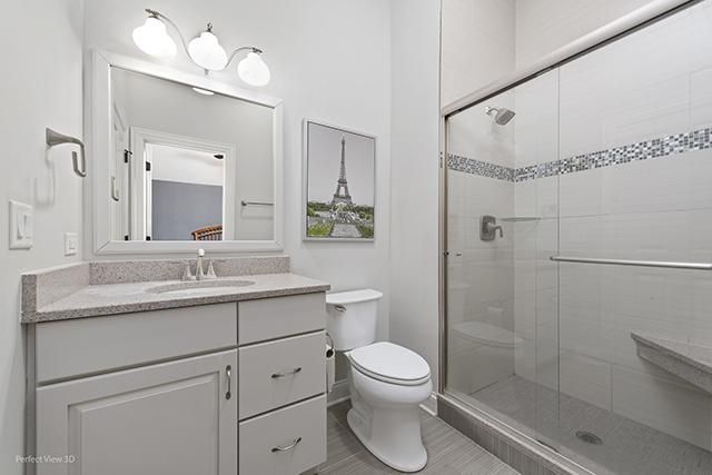 A bathroom with a toilet , sink , mirror and walk in shower.
