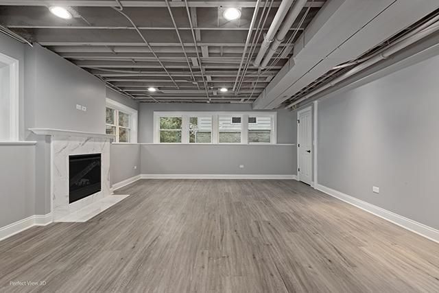 An empty basement with hardwood floors and a fireplace.