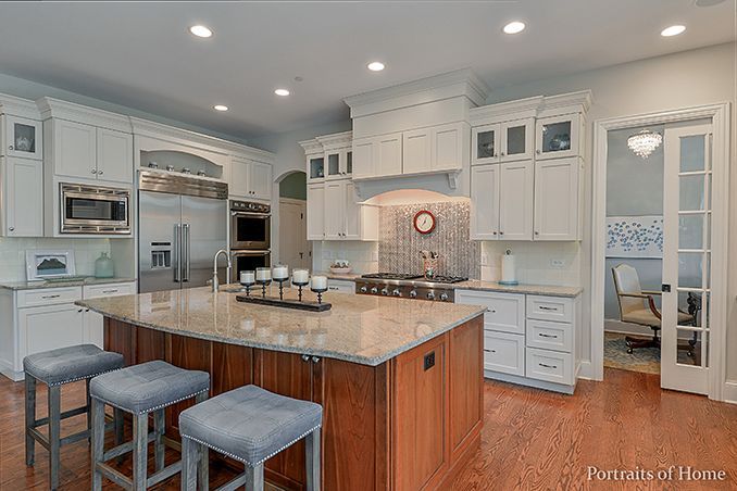 A kitchen with white cabinets , granite counter tops , stainless steel appliances and a large island.