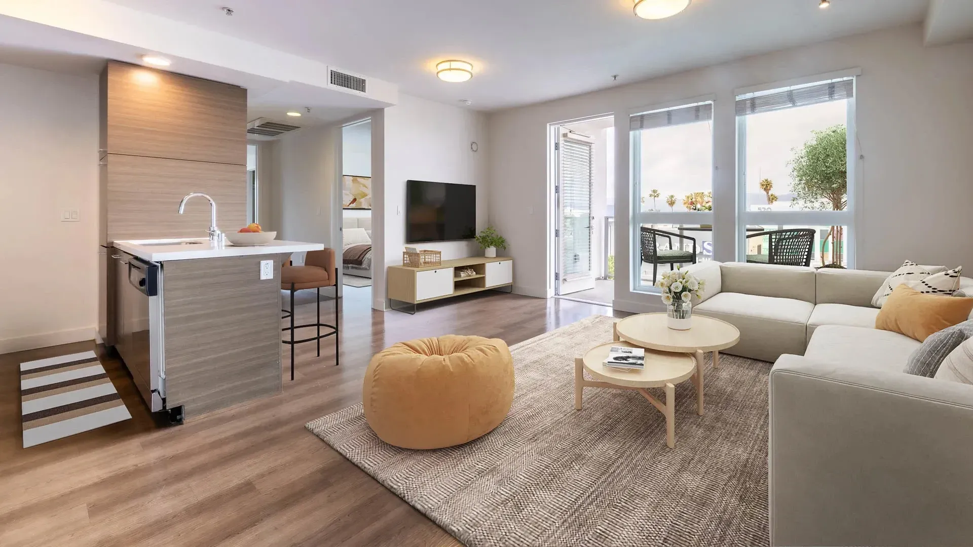 Modern living room and kitchen area with a sectional sofa, coffee tables, TV, and island at Next on Sixth Los Angeles