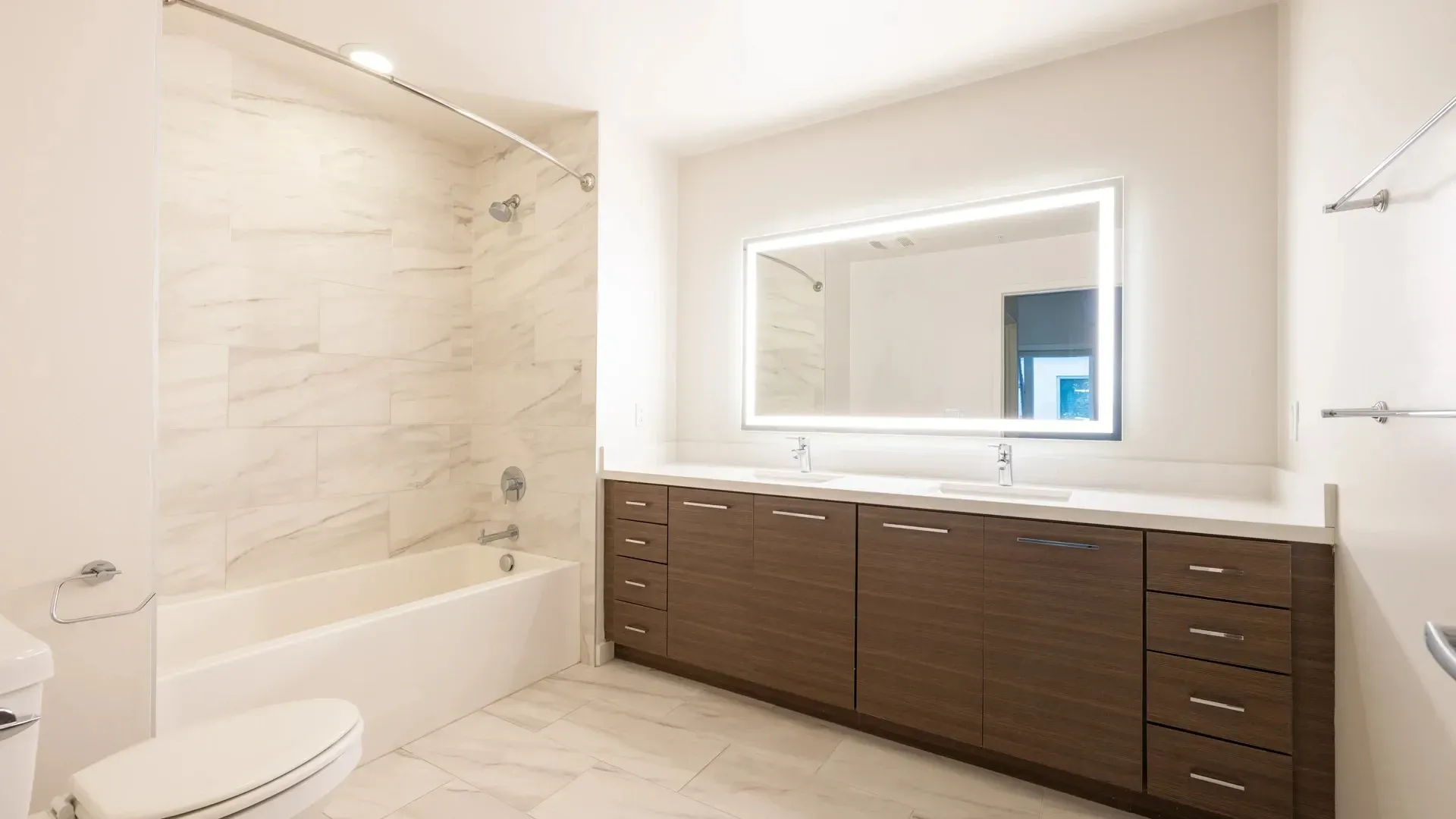 Modern bathroom with double vanity, large illuminated mirror, and bathtub at Next on Sixth Los Angeles