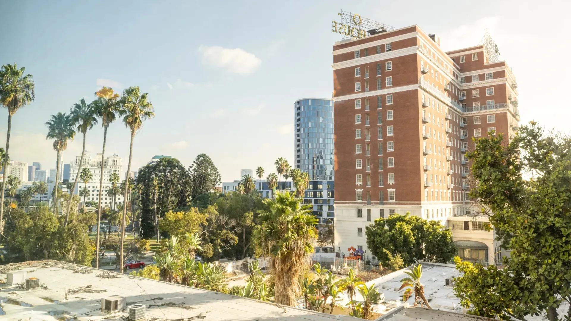 View of a historic brick building with a rooftop sign and palm trees, overlooking a city skyline at Next on Sixth Los Angeles