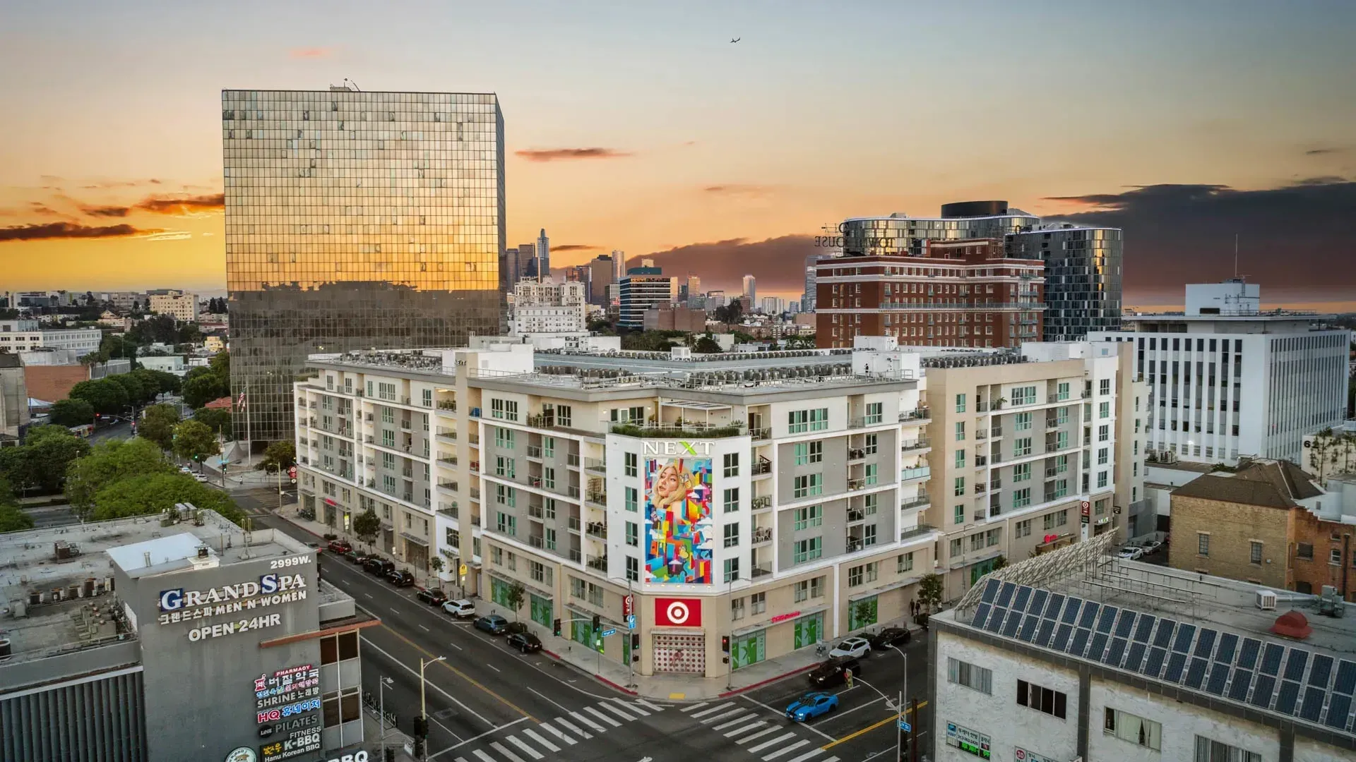 Aerial view of a modern apartment building with a colorful mural and Target store on the corner, during sunset at Next on Sixth Los Angeles
