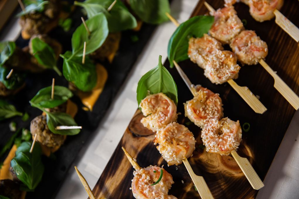 Brochettes de crevettes et amuse-bouche sur planches en bois, garnies de feuilles de basilic.