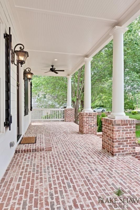 A brick porch with white columns and a ceiling fan