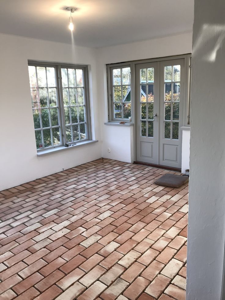 An empty room with a brick floor and two windows.