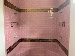 A shower stall with pink tiles and brown trim.