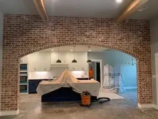 A kitchen with a brick wall and a vacuum cleaner on the floor.
