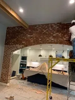 Two men are working on a brick wall in a kitchen.