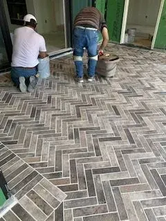 Two men are working on a herringbone tile floor.