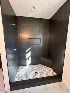 A walk in shower with black tiles and a white tile floor.