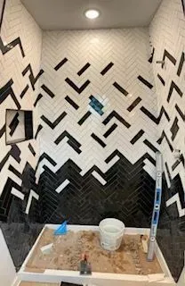 A bathroom with a black and white herringbone tile wall.