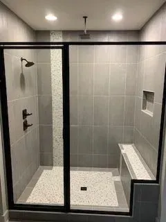 A walk in shower with a bench and a shower head.