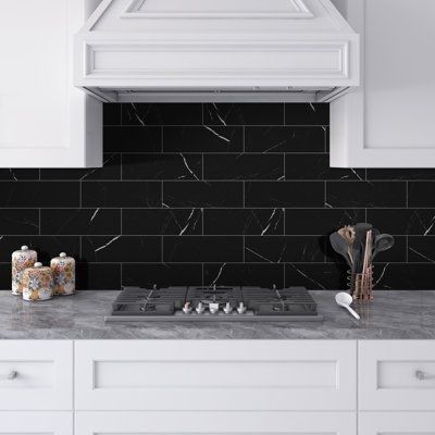 A kitchen with black subway tiles on the wall and a stove top oven.