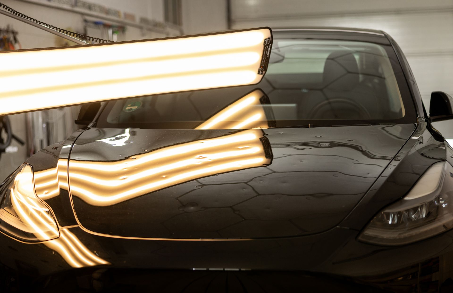 A black car hood under inspection lights, showing reflections and surface texture for paint or dent repair.
