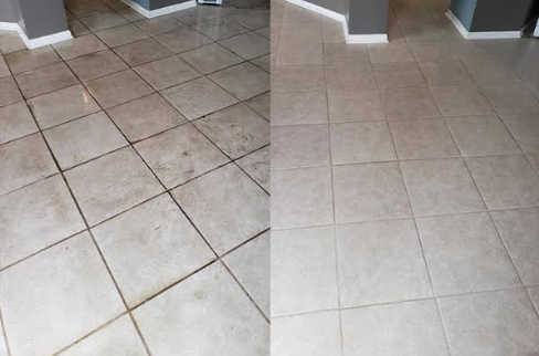 Hand using a trowel to apply grout between gray patterned floor tiles.