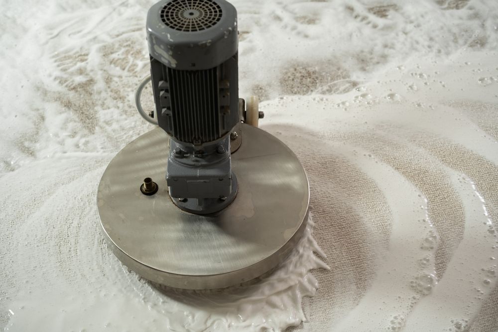 Large industrial floor cleaner with spinning circular brush, creating foamy suds on a floor.