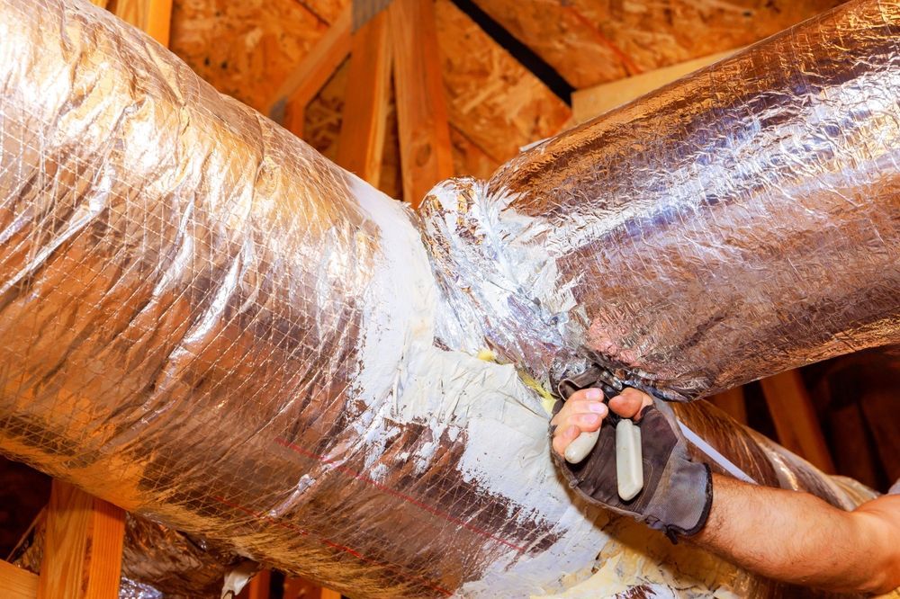 Person repairing HVAC ductwork in an attic, using pliers and sealant. Silver ducts, wood beams.