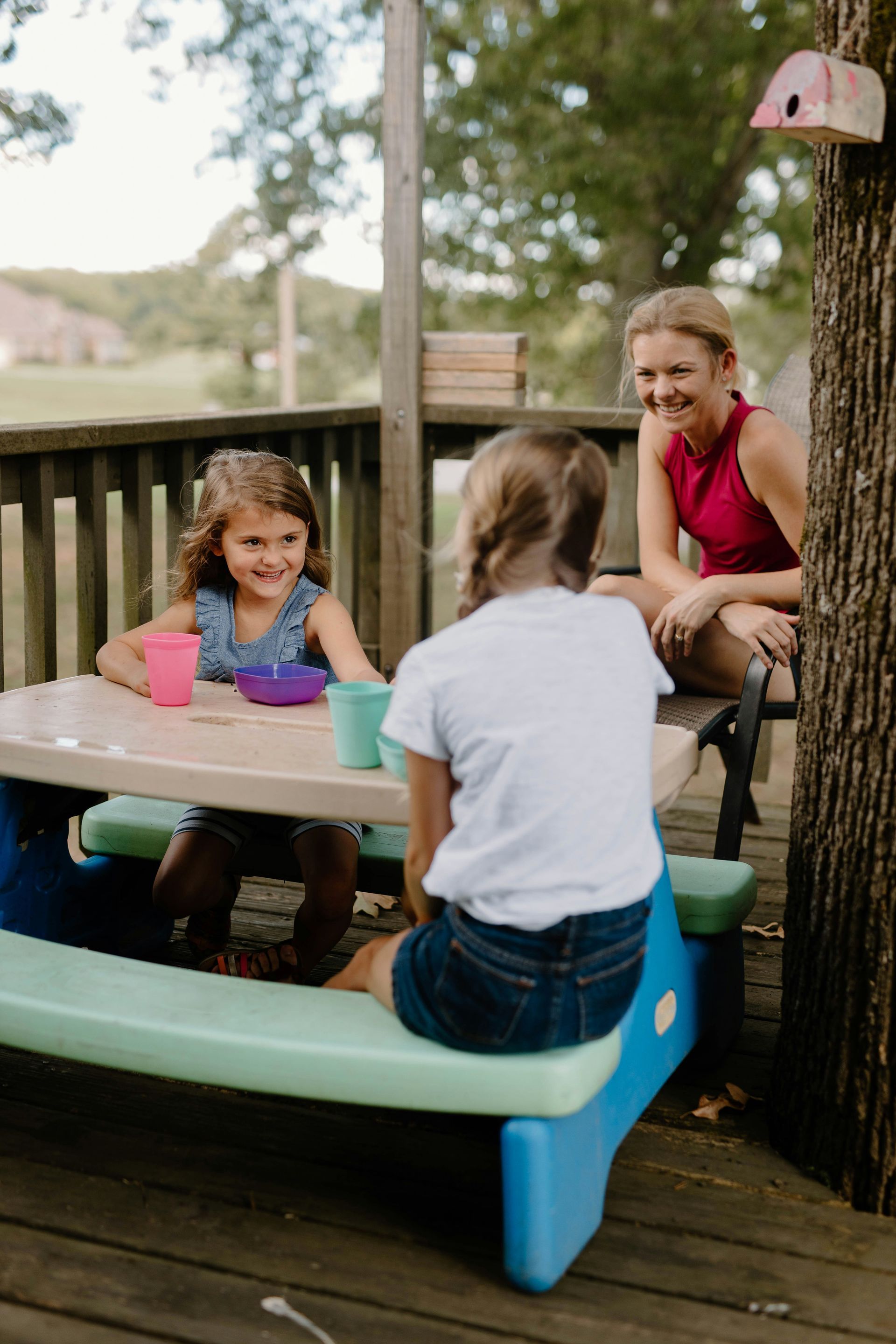 A woman and two girls are sitting at a picnic table on a deck.