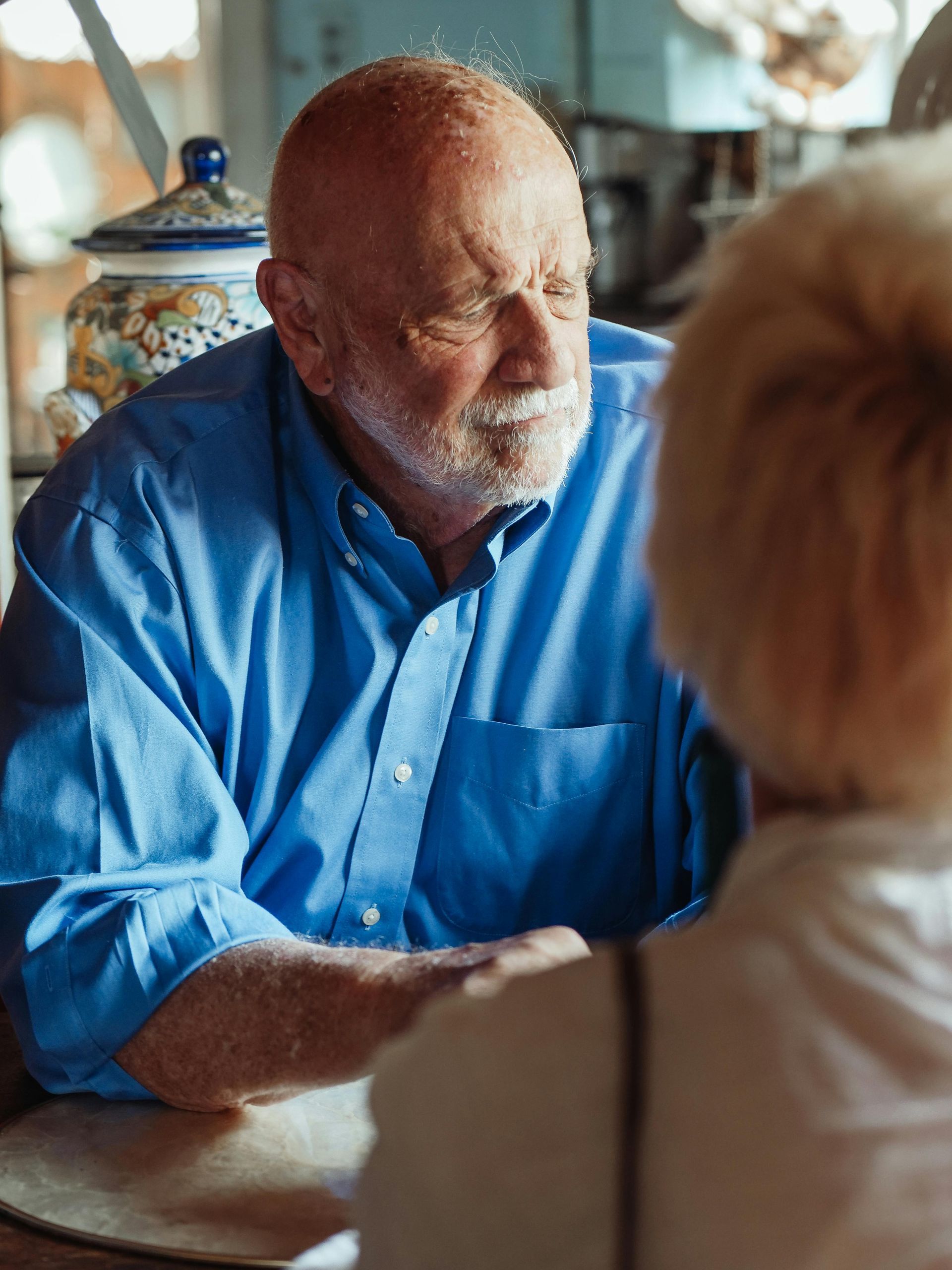 A man in a blue shirt is sitting at a table talking to a woman.