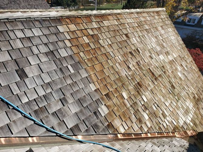 A cedar shake roof showing a contrast between weathered grey shingles on the left and cleaned, natural wood on the right.
