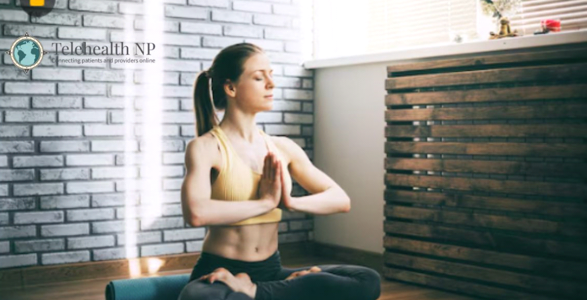 Woman in yoga pose with hands together, eyes closed, in a sunlit room.