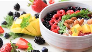 Bowl of mixed berries, mango, and almonds, with berries scattered around.