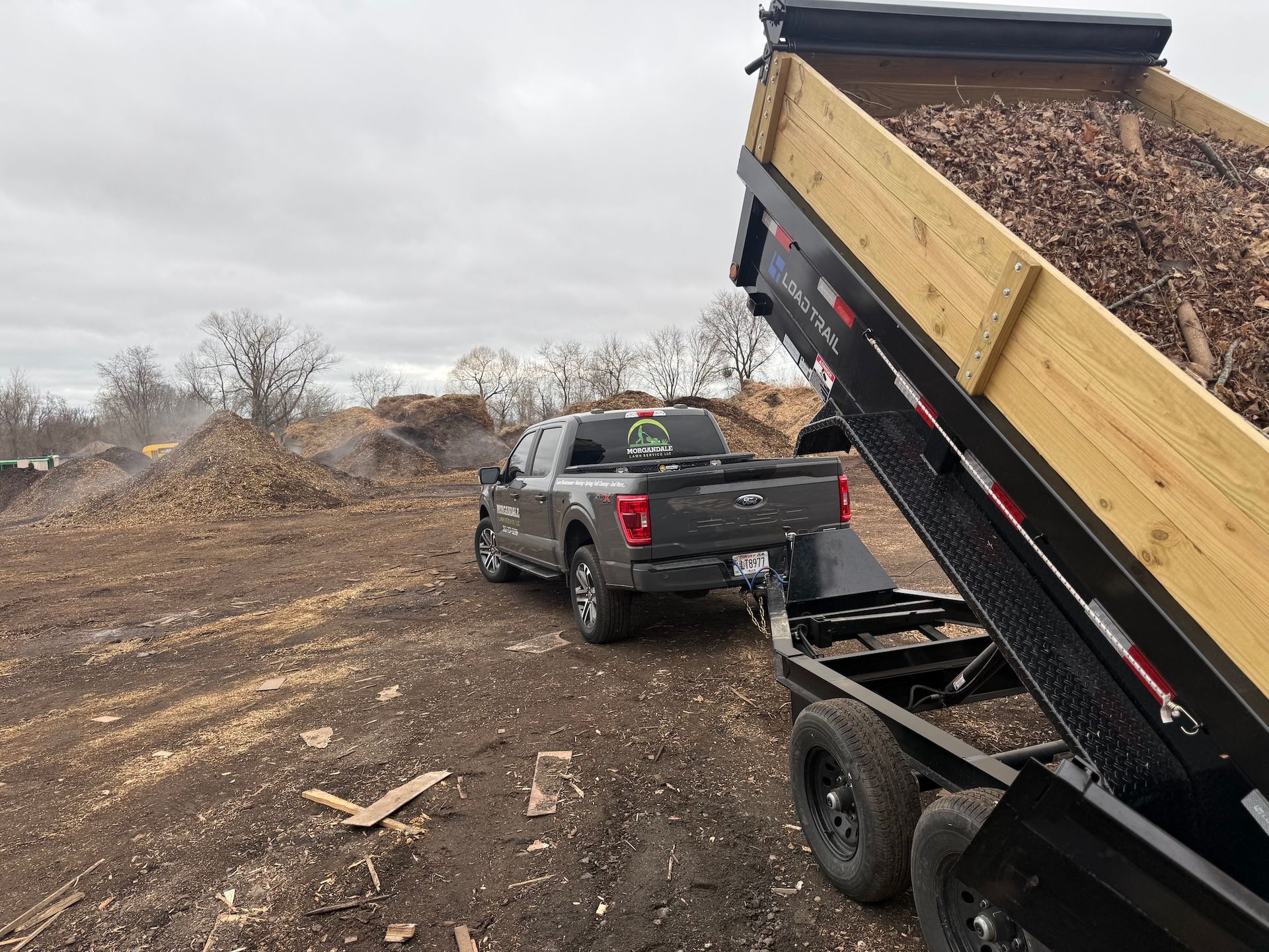 Pickup truck loading dirt into a dump trailer at a muddy construction site