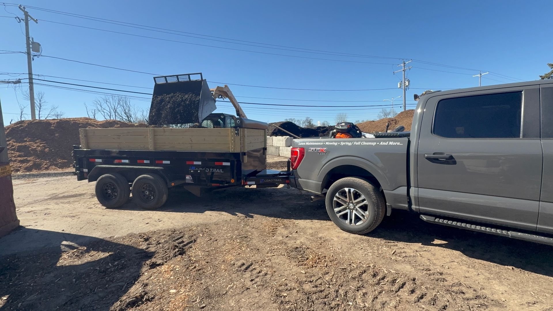 Gray pickup towing a utility trailer with equipment through a dusty construction area