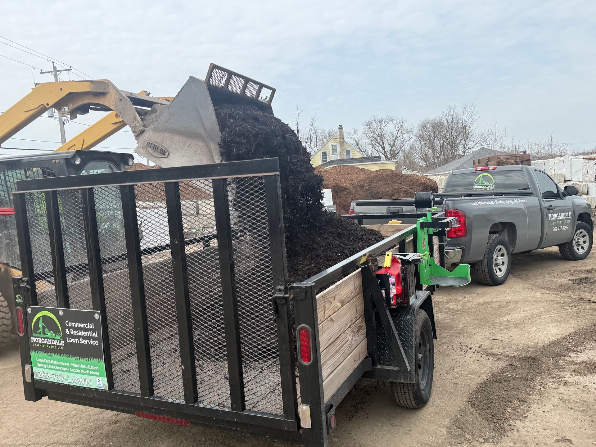 Dump trailer filled with dark gravel at a construction site beside a gray pickup truck