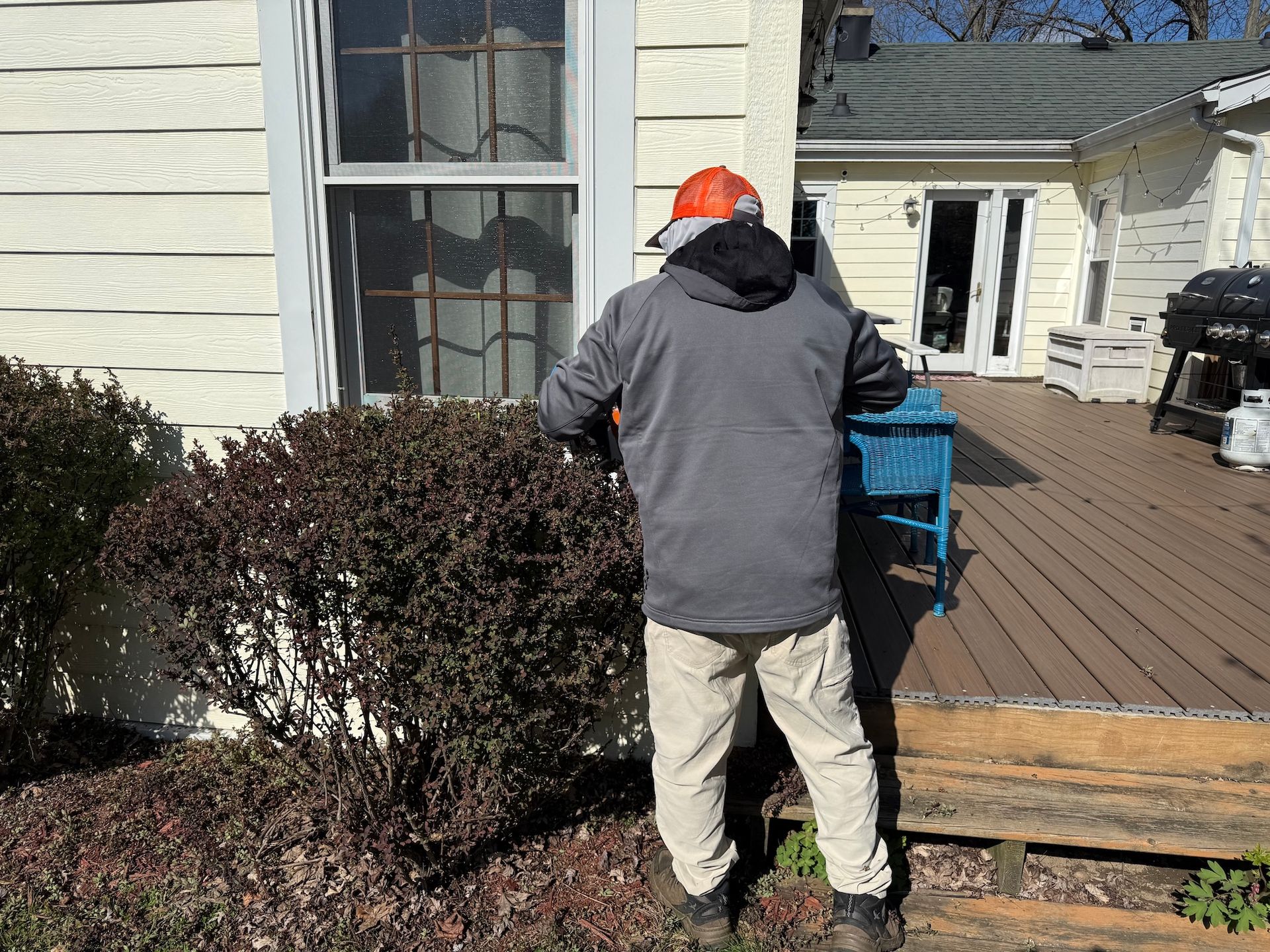 Worker in orange hard hat handling a blue machine beside a house and deck outdoors