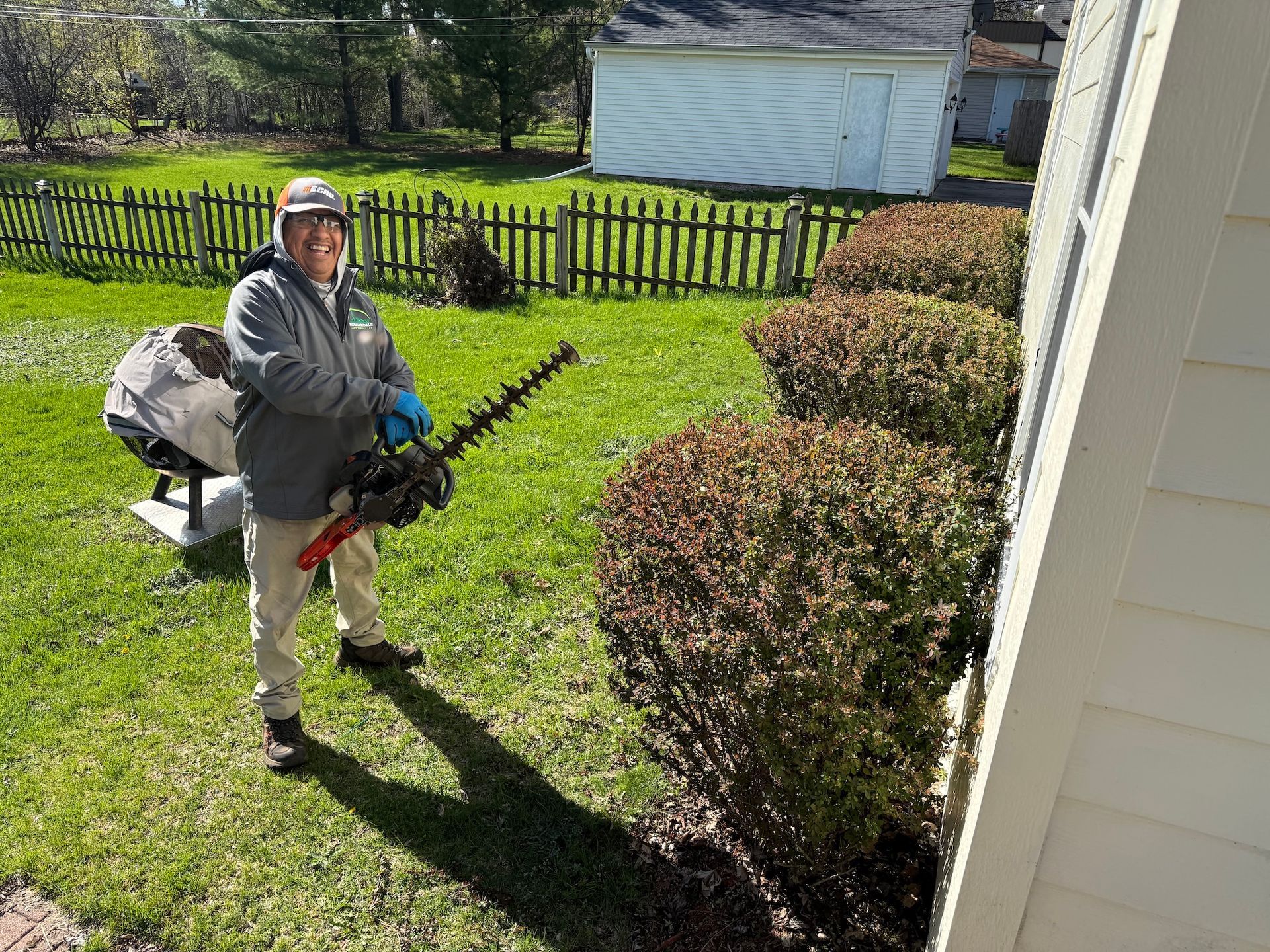 Person using a hedge trimmer beside trimmed bushes in a sunny yard