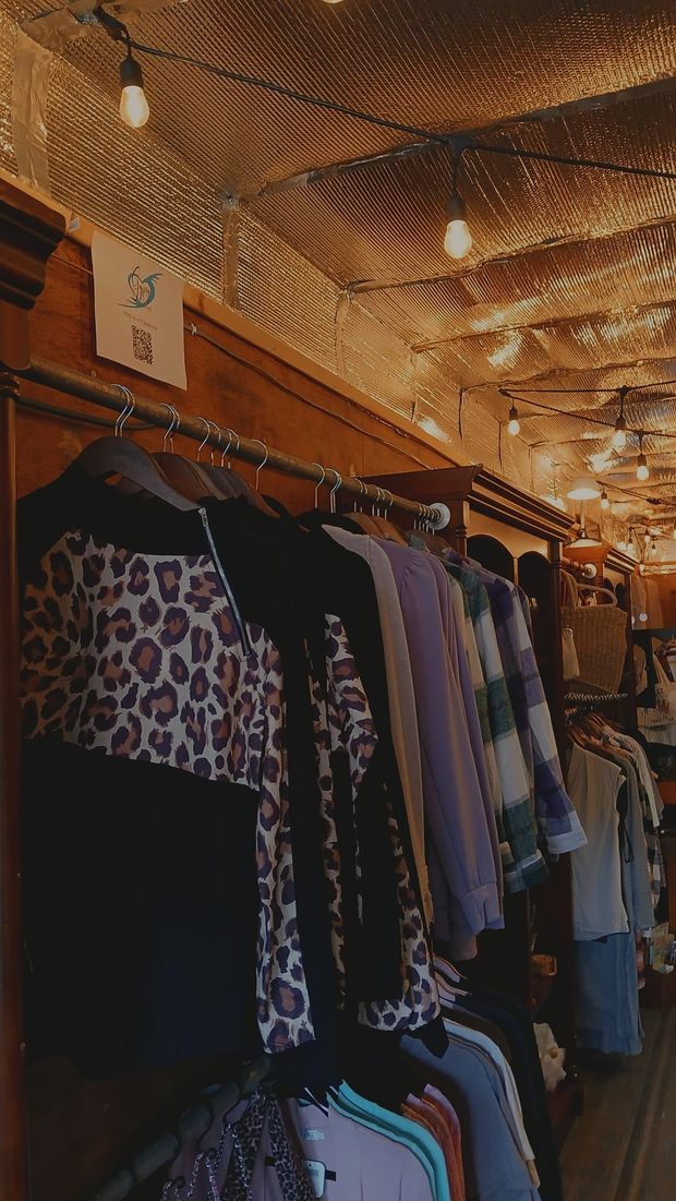 Clothing on a rack inside a dimly lit boutique with a textured ceiling, string lights, and a hanging sale sign.