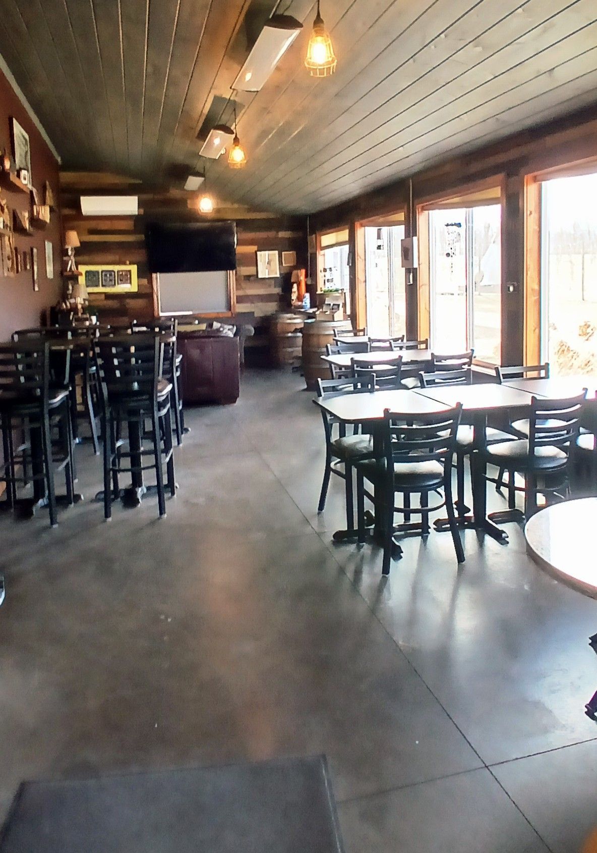 Dimly lit restaurant interior with dark wooden walls, multiple round tables, and black chairs.