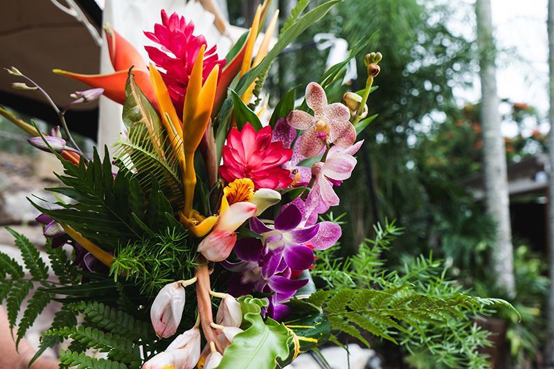Vibrant bouquet of tropical flowers: orange, red, pink, and purple orchids with green foliage, outside.